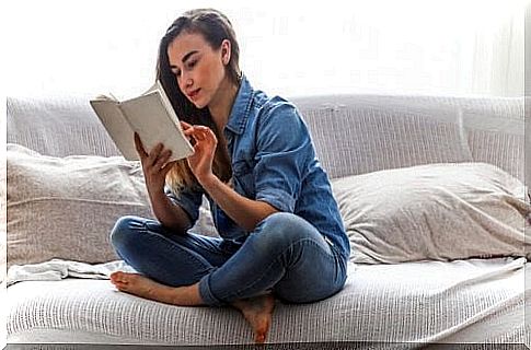 A woman is sitting and reading on the bed