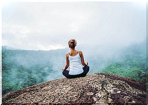 A woman is sitting and meditating on a rock