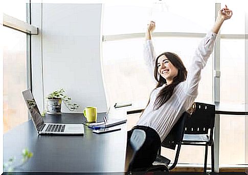 Smiling woman with arms over head in office