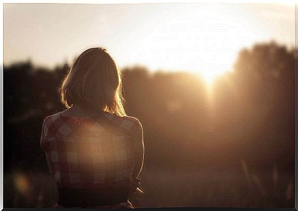 Woman standing alone in field watching sunset